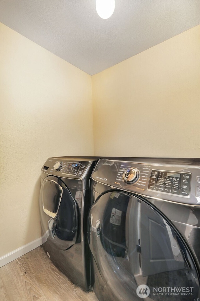 clothes washing area with washer and clothes dryer, wood finished floors, and baseboards
