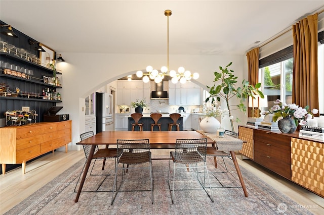 dining space featuring light wood-style floors, arched walkways, and a chandelier