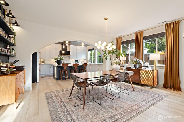 dining area with arched walkways, a chandelier, and light wood-style flooring