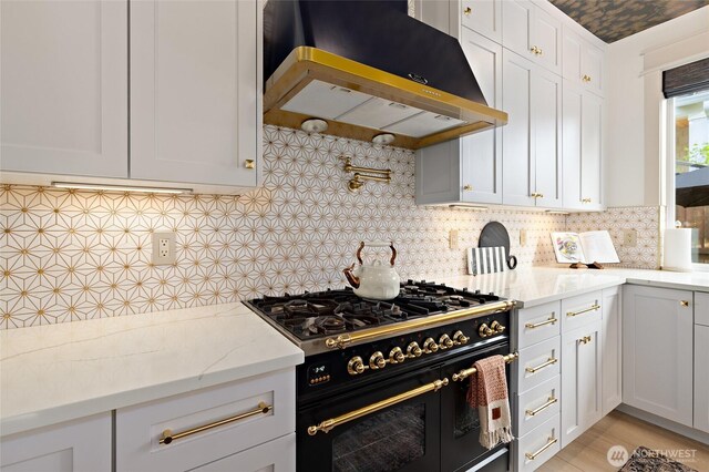 kitchen featuring double oven range, ventilation hood, backsplash, light stone countertops, and white cabinetry
