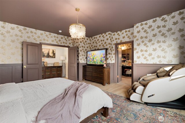 bedroom with wallpapered walls, wainscoting, a chandelier, connected bathroom, and light wood-style flooring