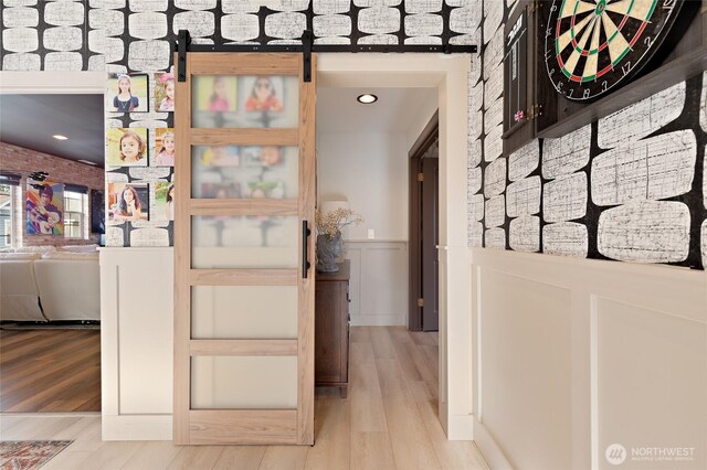 hallway with a wainscoted wall, wood finished floors, a barn door, and a decorative wall
