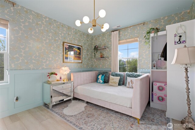 bedroom with wallpapered walls, wainscoting, multiple windows, and a chandelier