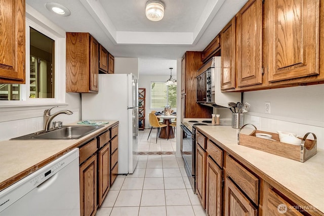 kitchen featuring white appliances, a sink, brown cabinetry, a raised ceiling, and light countertops