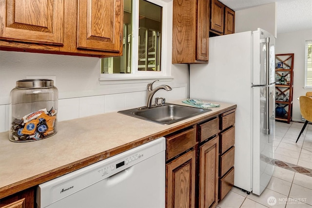 kitchen with white dishwasher, a sink, brown cabinetry, and light tile patterned floors