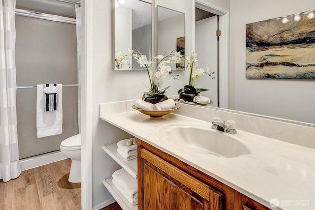 bathroom featuring wood finished floors, a stall shower, toilet, and vanity