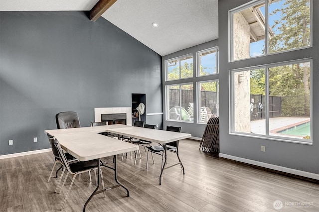 dining area with high vaulted ceiling, beam ceiling, wood finished floors, a tile fireplace, and baseboards