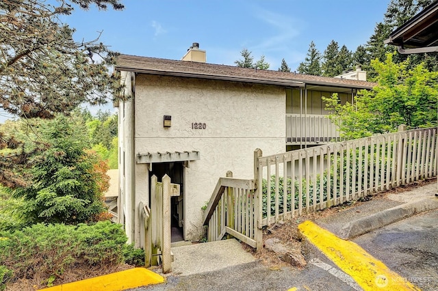 exterior space featuring stucco siding, a chimney, and fence