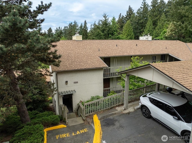 view of front of house with a shingled roof, a chimney, and fence