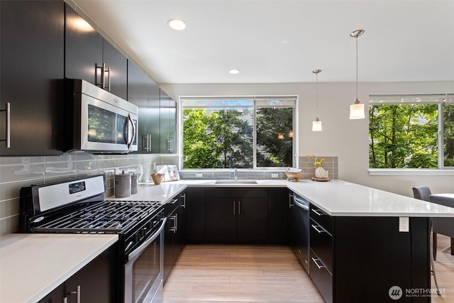 kitchen featuring appliances with stainless steel finishes, a peninsula, light countertops, light wood-type flooring, and recessed lighting