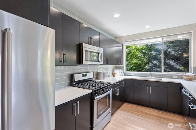 kitchen featuring appliances with stainless steel finishes, light wood finished floors, light countertops, decorative backsplash, and a sink