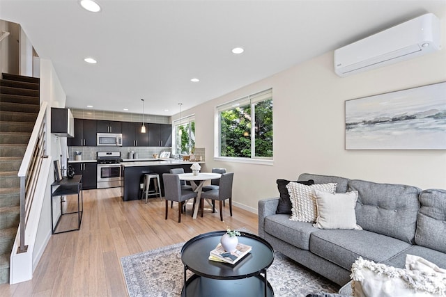 living area featuring an AC wall unit, stairs, light wood-style floors, recessed lighting, and baseboards