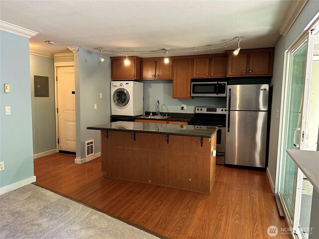 kitchen featuring washer / clothes dryer, stainless steel appliances, a sink, a kitchen island, and dark wood-style floors