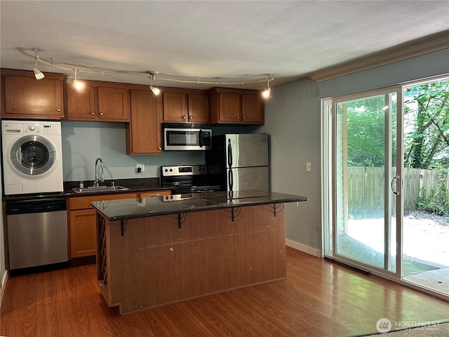 kitchen featuring washer / dryer, stainless steel appliances, a sink, a breakfast bar area, and dark wood-type flooring