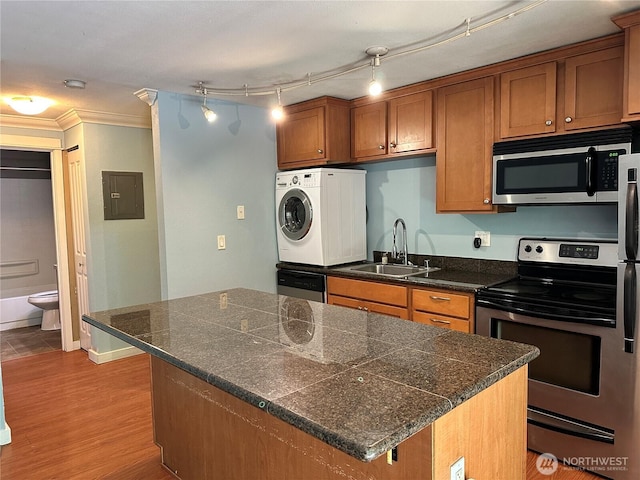 kitchen with appliances with stainless steel finishes, washer / dryer, a sink, brown cabinetry, and tile countertops
