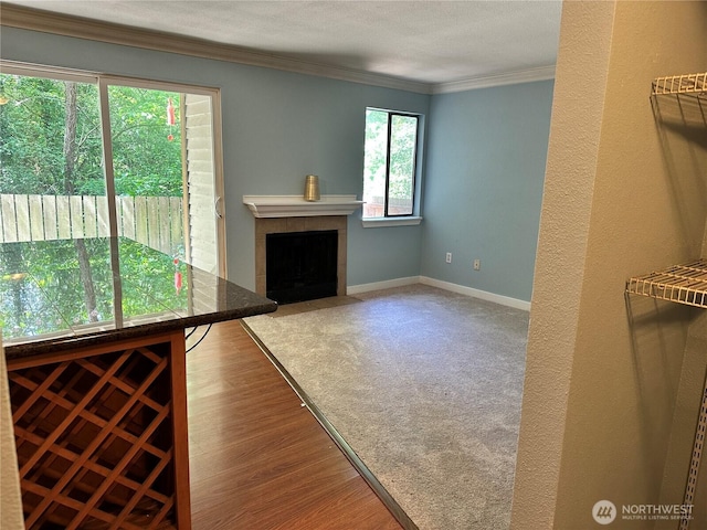 unfurnished living room featuring ornamental molding, a tile fireplace, baseboards, and wood finished floors