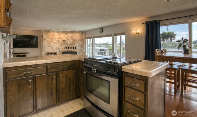 712 Mt Olympus Ave SE, Ocean Shores, WA 98569 - kitchen featuring electric stove, tile counters, plenty of natural light, a textured ceiling, and a stone fireplace
