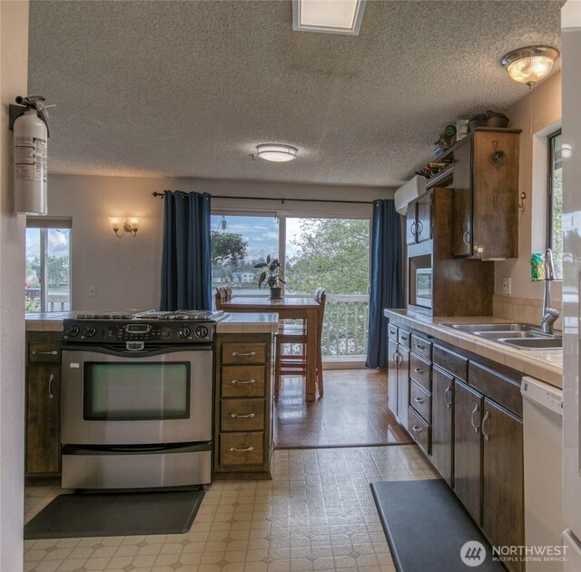 712 Mt Olympus Ave SE, Ocean Shores, WA 98569 - kitchen with stainless steel range with gas stovetop, dishwasher, tile counters, a sink, and a textured ceiling