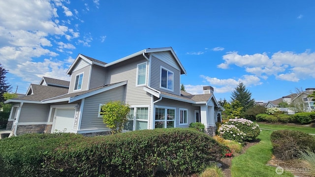 view of home's exterior with a chimney, an attached garage, a shingled roof, and stone siding
