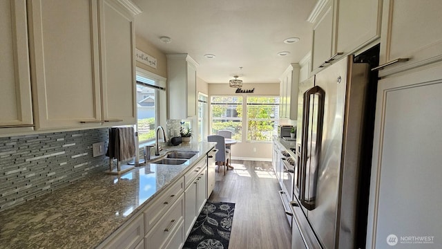 kitchen featuring appliances with stainless steel finishes, a sink, dark wood-style flooring, tasteful backsplash, and dark stone countertops