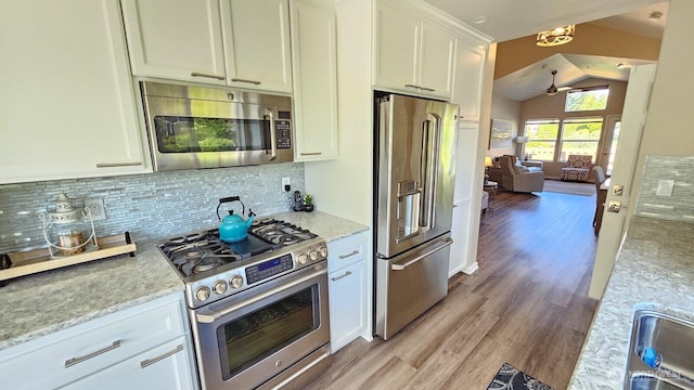 kitchen featuring appliances with stainless steel finishes, ceiling fan, light wood finished floors, decorative backsplash, and vaulted ceiling