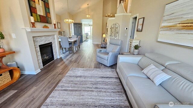 living room with wood finished floors, baseboards, high vaulted ceiling, and a glass covered fireplace