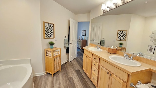 full bath featuring wood finished floors, double vanity, a bath, and baseboards