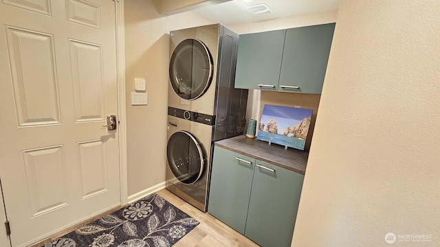 clothes washing area featuring stacked washer / drying machine, cabinet space, light wood finished floors, and baseboards