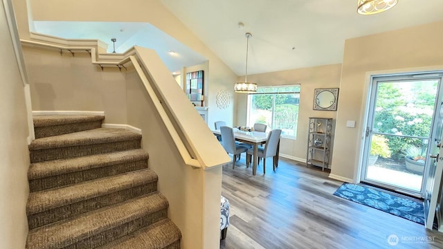 stairs with a chandelier, wood finished floors, lofted ceiling, and baseboards