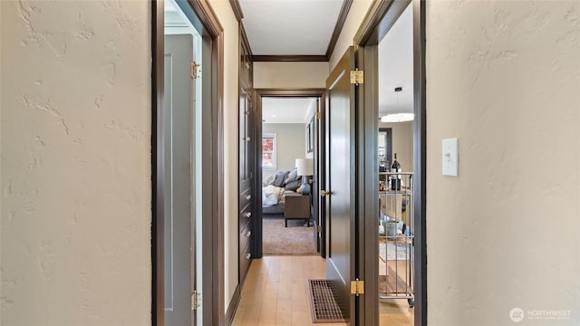 hallway featuring ornamental molding, light wood finished floors, and a textured wall