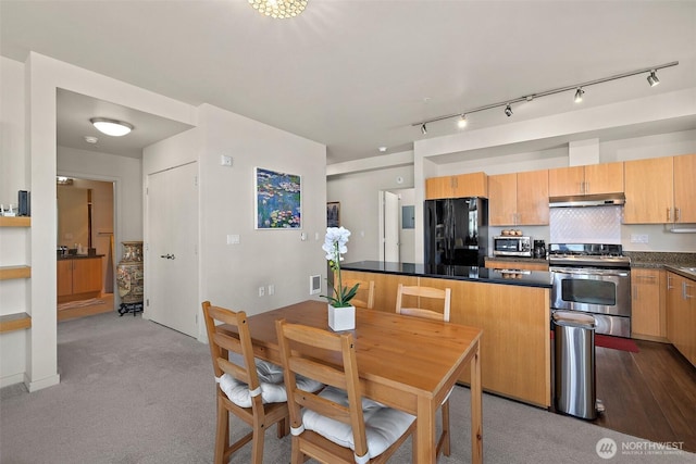 kitchen featuring stainless steel range with gas stovetop, freestanding refrigerator, under cabinet range hood, dark countertops, and carpet