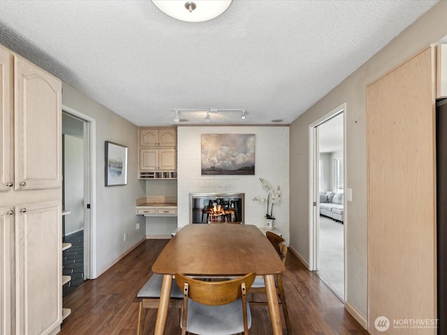 dining space featuring dark wood-style flooring, a glass covered fireplace, a textured ceiling, and baseboards