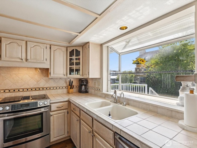 kitchen featuring stainless steel electric range oven, tile countertops, a sink, light brown cabinetry, and tasteful backsplash
