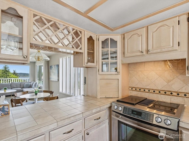 kitchen featuring stainless steel electric stove, tile countertops, glass insert cabinets, decorative backsplash, and light brown cabinetry
