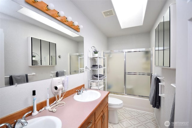 bathroom featuring a skylight, bath / shower combo with glass door, tile patterned floors, double vanity, and toilet