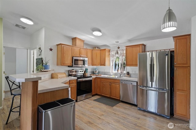 kitchen with stainless steel appliances, a peninsula, light wood-style floors, and hanging light fixtures