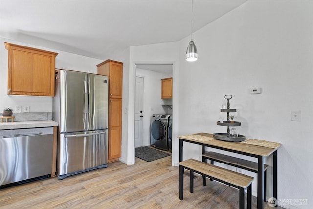 kitchen featuring stainless steel appliances, washer and dryer, light wood-type flooring, light countertops, and brown cabinets