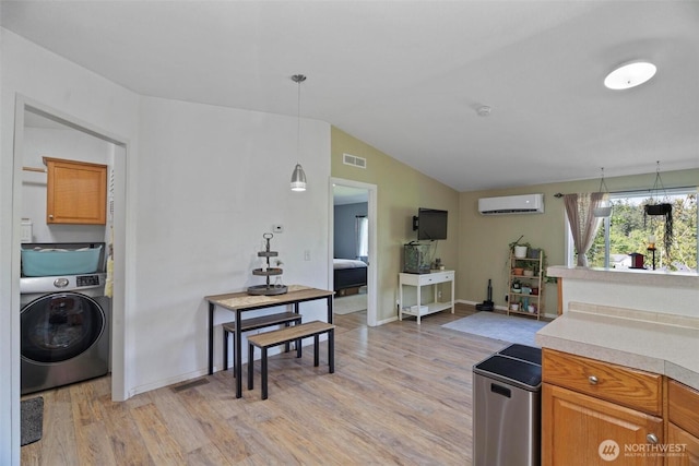 kitchen with washer / dryer, a wall mounted AC, light wood-type flooring, light countertops, and vaulted ceiling