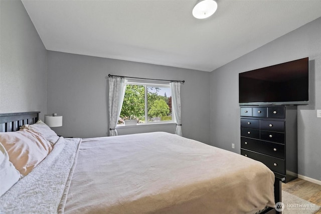 bedroom with wood finished floors, baseboards, and vaulted ceiling