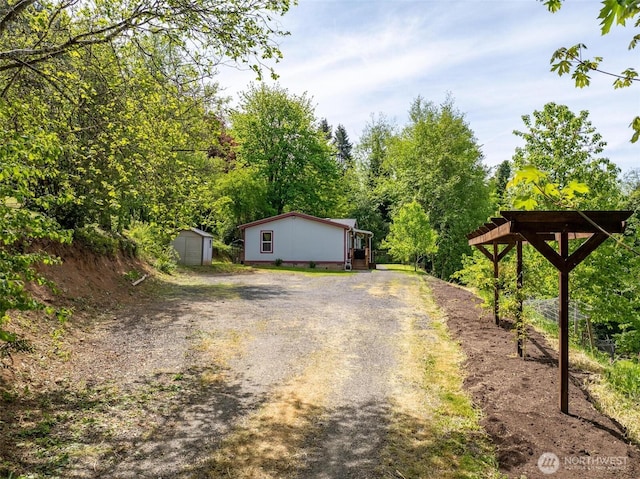 view of side of property with driveway, a storage unit, and an outbuilding
