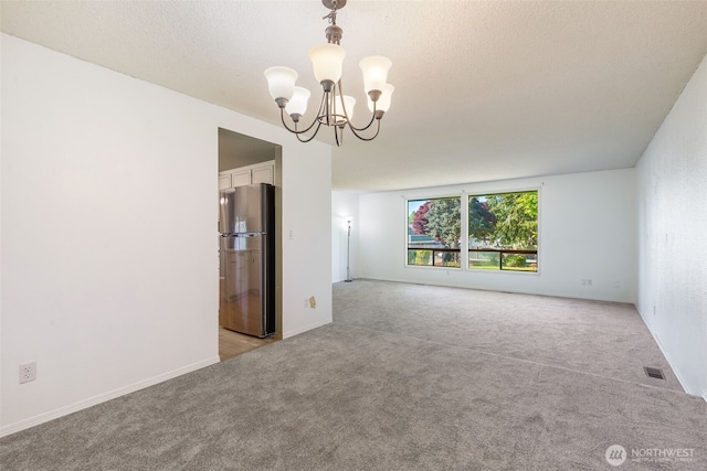 unfurnished room with light colored carpet, a chandelier, baseboards, and a textured ceiling