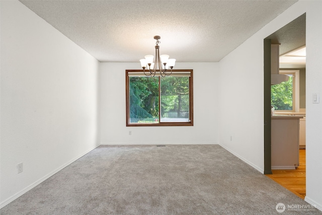 carpeted spare room featuring healthy amount of natural light, a chandelier, a textured ceiling, and baseboards