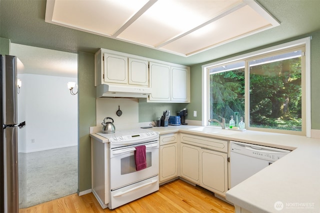 kitchen with white appliances, under cabinet range hood, a sink, light wood-style floors, and light countertops