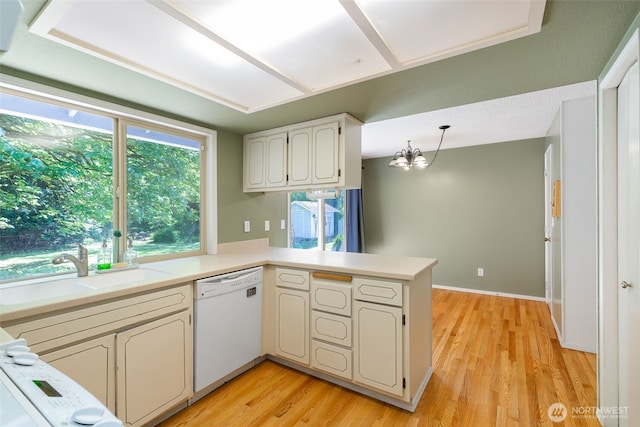 kitchen with white dishwasher, a sink, a peninsula, light wood-style flooring, and light countertops