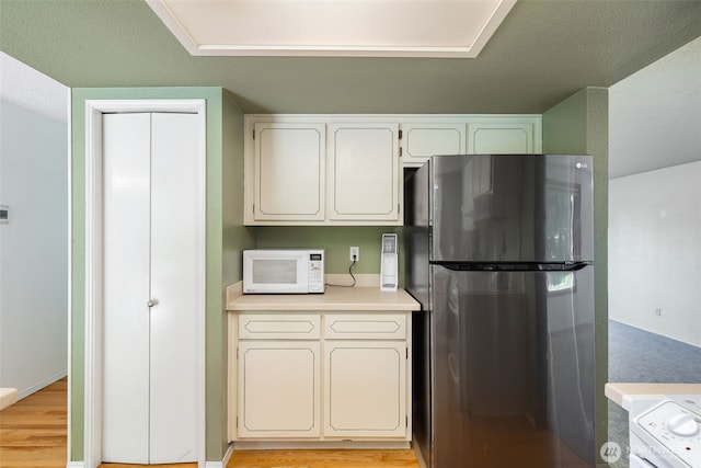 kitchen featuring freestanding refrigerator, white microwave, light countertops, white cabinetry, and light wood-type flooring