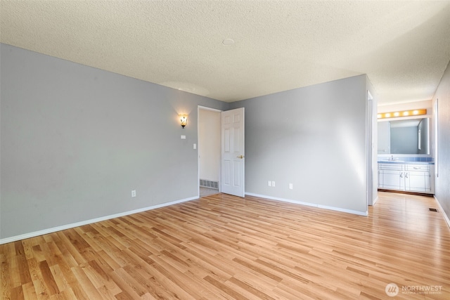 empty room featuring a textured ceiling, light wood finished floors, and baseboards