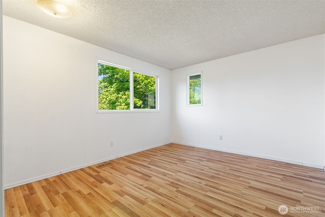 unfurnished room featuring light wood-type flooring, baseboards, and a textured ceiling