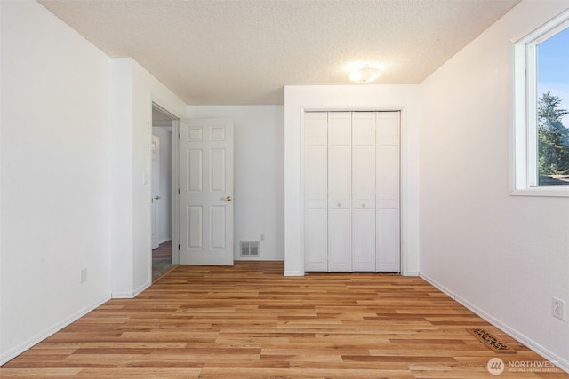 unfurnished bedroom with light wood-style floors, multiple windows, a closet, baseboards, and a textured ceiling