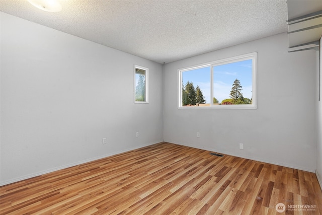spare room featuring light wood-style floors, a textured ceiling, and baseboards