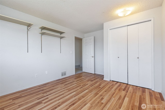 unfurnished bedroom featuring light wood-style flooring, a textured ceiling, a closet, and baseboards